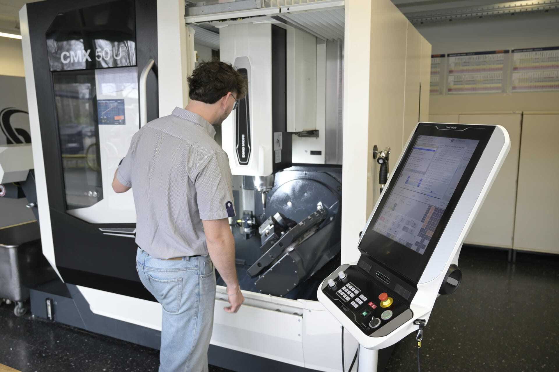 Ein junger Mann steht vor einer CNC-Maschine und beobachtet den Produktionsprozess.