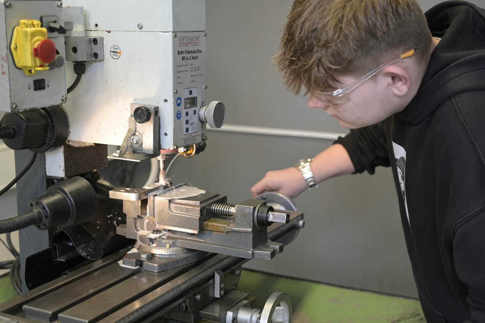 Ein Jugendlicher arbeitet an einer Bohr-Fräsmaschine. Er trägt Schutzbrille.