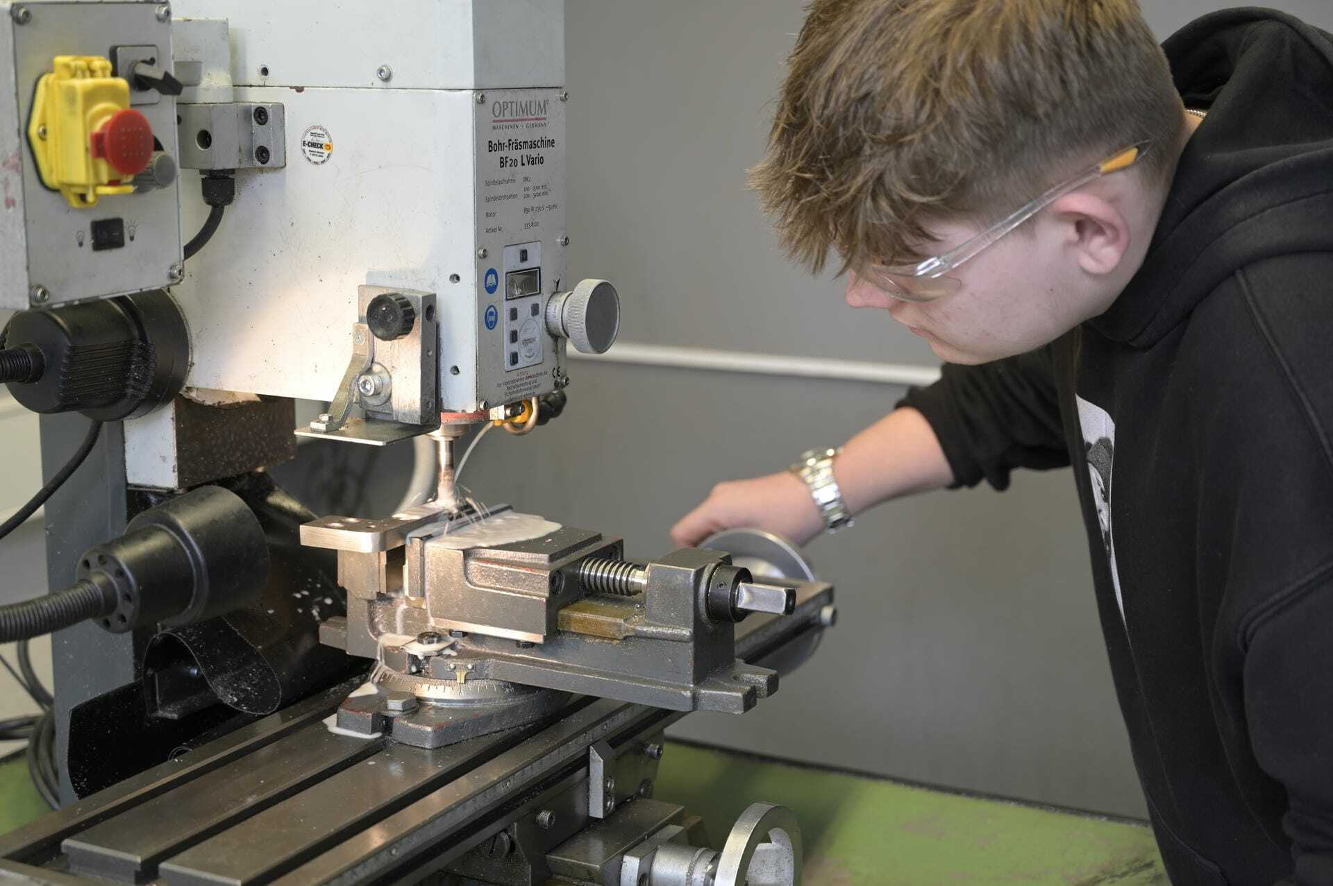 Ein junger Mann arbeitet an einer Fräsmaschine mit Schutzbrille.